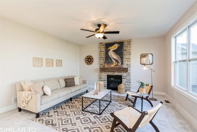 living room with ceiling fan, a stone fireplace, and light colored carpet