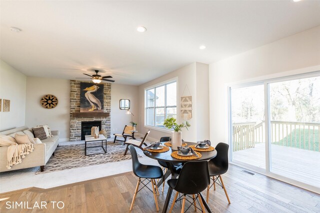 dining space with hardwood / wood-style floors, a stone fireplace, ceiling fan, and a healthy amount of sunlight