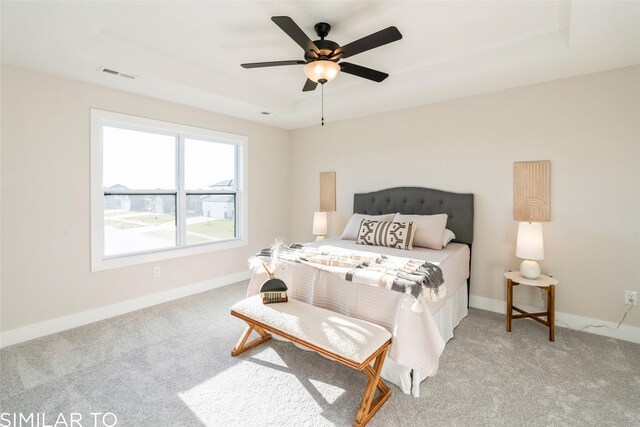 carpeted bedroom with ceiling fan and a raised ceiling