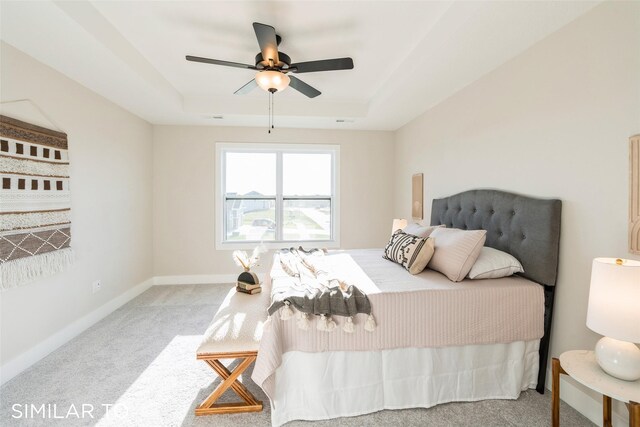 bedroom with a raised ceiling, ceiling fan, and light colored carpet