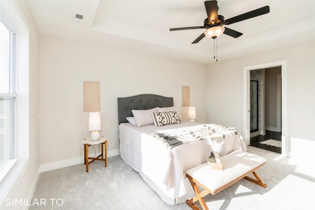 bedroom featuring light colored carpet, a raised ceiling, and ceiling fan