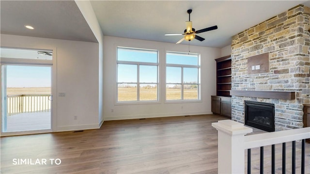 unfurnished living room featuring a stone fireplace, ceiling fan, hardwood / wood-style floors, and built in features