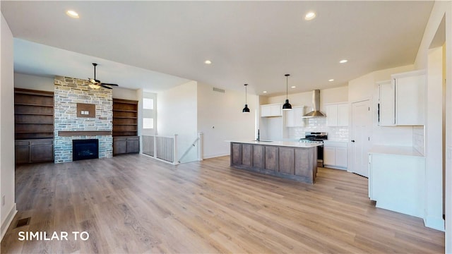 kitchen with light hardwood / wood-style flooring, stainless steel gas range, wall chimney exhaust hood, an island with sink, and white cabinetry