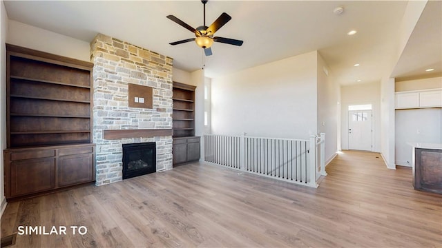 unfurnished living room featuring built in shelves, light hardwood / wood-style floors, a fireplace, and ceiling fan