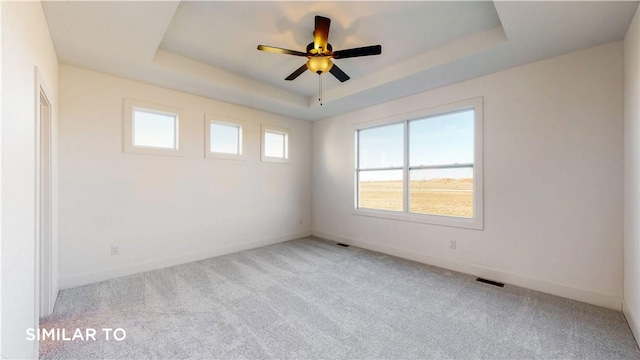 carpeted spare room with a tray ceiling and ceiling fan