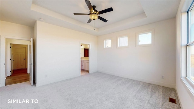 unfurnished bedroom with a tray ceiling, multiple windows, and ceiling fan