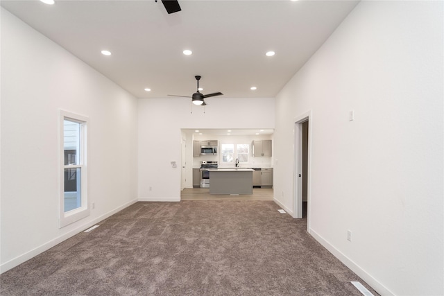 unfurnished living room with carpet, ceiling fan, and sink