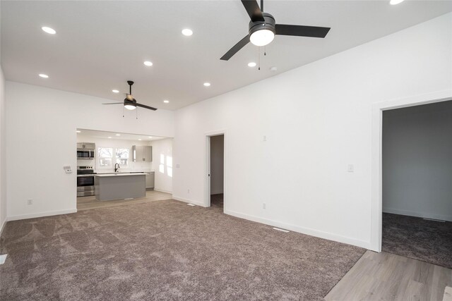 unfurnished living room featuring wood-type flooring, ceiling fan, and sink