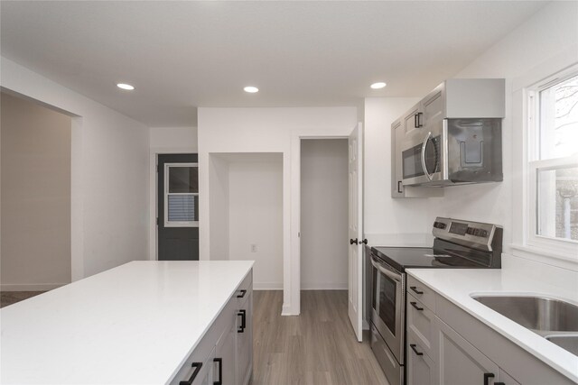 kitchen featuring appliances with stainless steel finishes, light wood-type flooring, gray cabinets, and sink