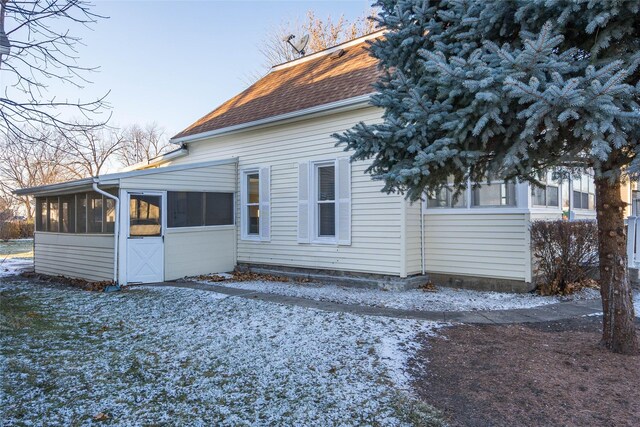 snow covered rear of property with a sunroom