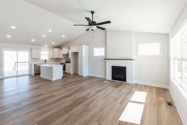 unfurnished living room featuring light wood-style floors, a glass covered fireplace, visible vents, and baseboards