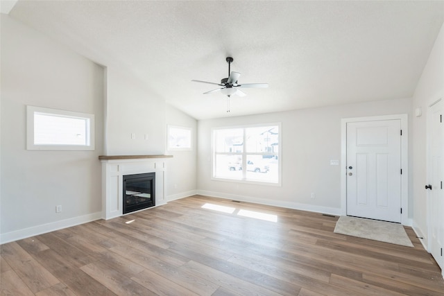 unfurnished living room with a wealth of natural light, a glass covered fireplace, and light wood-style flooring