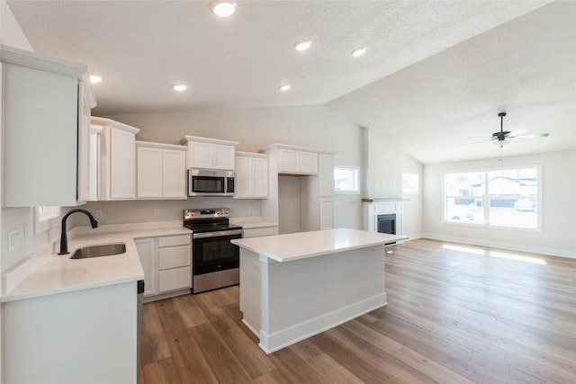 kitchen with white cabinets, appliances with stainless steel finishes, open floor plan, a center island, and a sink