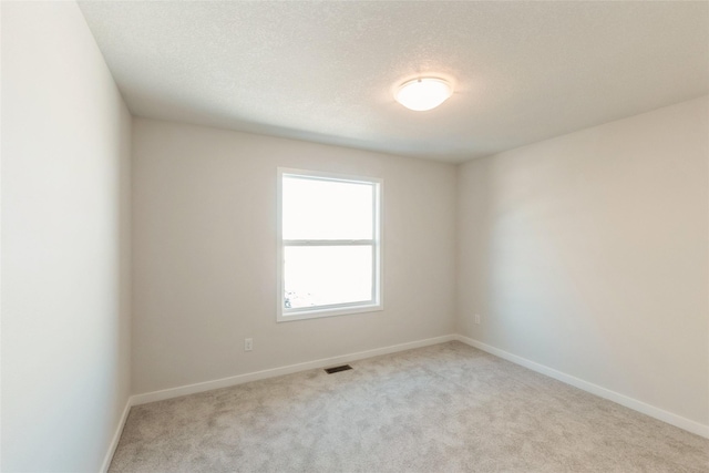 unfurnished room featuring baseboards, visible vents, a textured ceiling, and light colored carpet