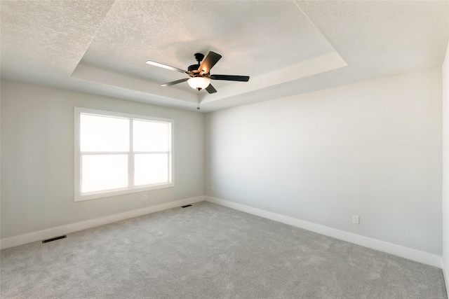 empty room featuring baseboards, visible vents, a tray ceiling, and a textured ceiling