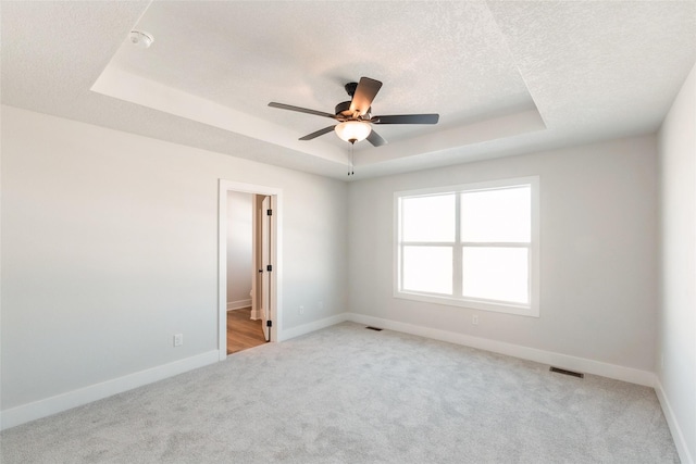 empty room featuring a raised ceiling, a textured ceiling, and baseboards