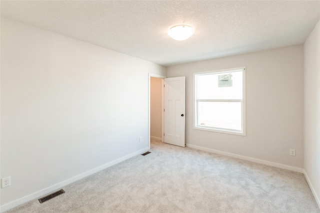 empty room with a textured ceiling, light colored carpet, visible vents, and baseboards