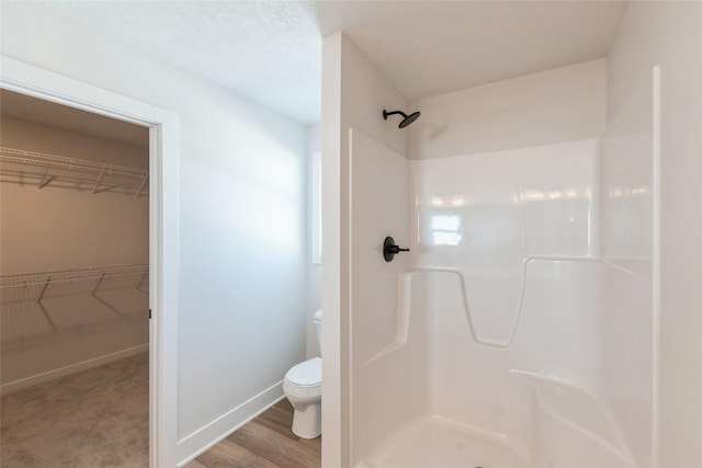 full bath with toilet, wood finished floors, baseboards, a spacious closet, and a stall shower