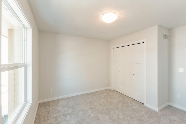 unfurnished bedroom featuring baseboards, a closet, visible vents, and light colored carpet