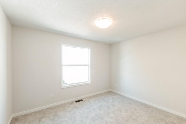 empty room with baseboards, visible vents, a textured ceiling, and light colored carpet