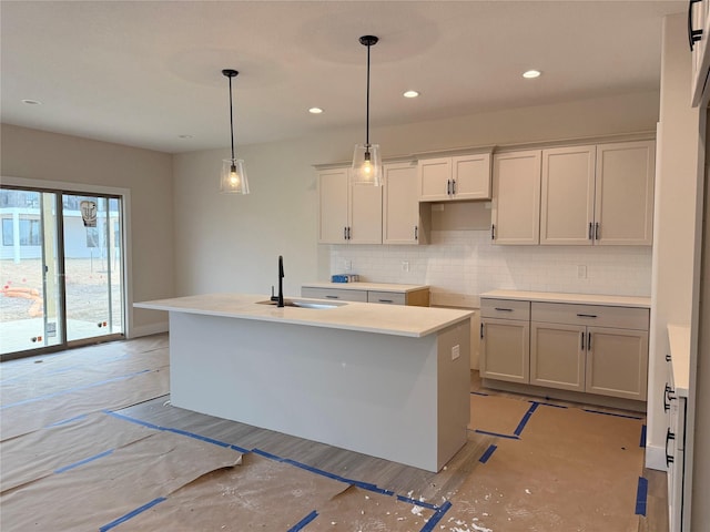 kitchen featuring decorative light fixtures, an island with sink, sink, white cabinets, and decorative backsplash