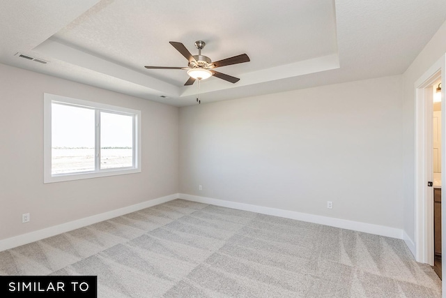 carpeted empty room with ceiling fan and a raised ceiling