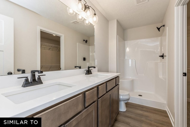 bathroom with walk in shower, a textured ceiling, toilet, vanity, and hardwood / wood-style flooring