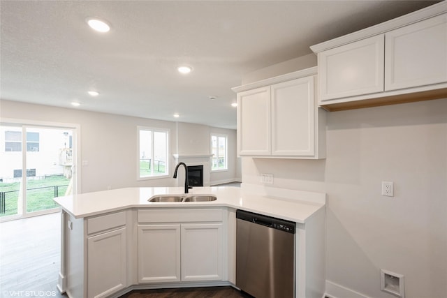 kitchen with stainless steel dishwasher, white cabinets, a sink, light countertops, and a peninsula
