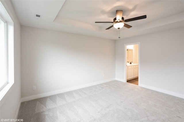 carpeted empty room with ceiling fan, a raised ceiling, and baseboards