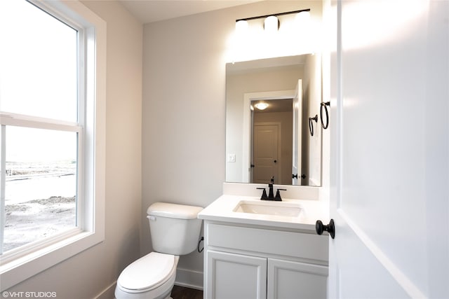 half bath featuring a healthy amount of sunlight, toilet, and vanity