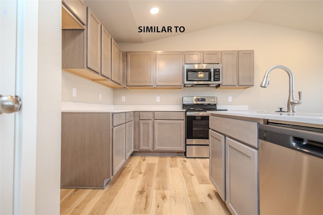 kitchen with light hardwood / wood-style floors, light brown cabinetry, appliances with stainless steel finishes, and vaulted ceiling