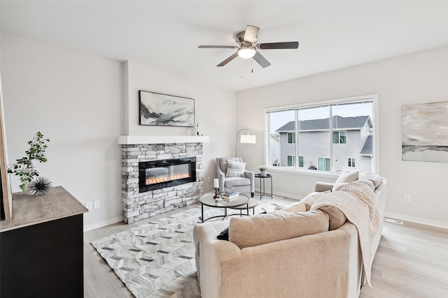 living room with a stone fireplace, ceiling fan, and light hardwood / wood-style flooring