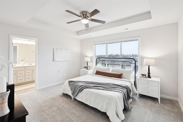 bedroom featuring light carpet, a tray ceiling, ceiling fan, and ensuite bathroom