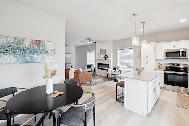 kitchen featuring pendant lighting, a center island, a large fireplace, white cabinetry, and stainless steel appliances