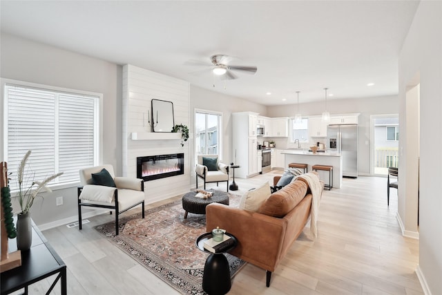 living room with a fireplace, light wood-type flooring, a healthy amount of sunlight, and sink