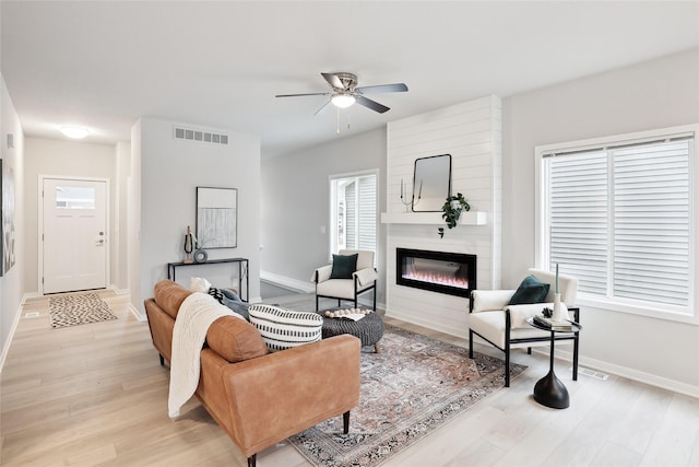 living room featuring a fireplace, light wood-type flooring, and ceiling fan