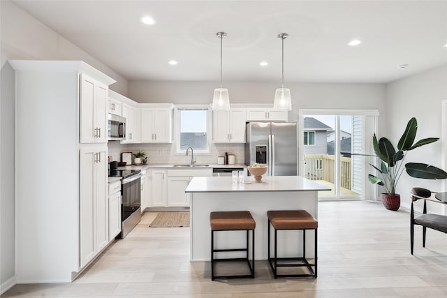 kitchen with stainless steel appliances, sink, a center island, white cabinetry, and hanging light fixtures