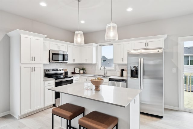 kitchen with appliances with stainless steel finishes, a breakfast bar, a kitchen island, white cabinetry, and hanging light fixtures