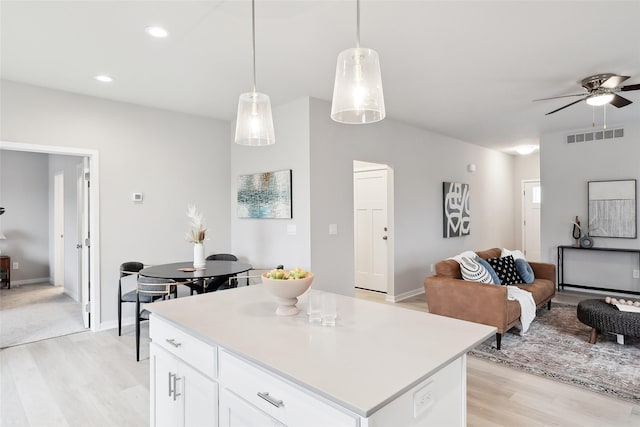 kitchen featuring ceiling fan, a kitchen island, decorative light fixtures, white cabinets, and light wood-type flooring