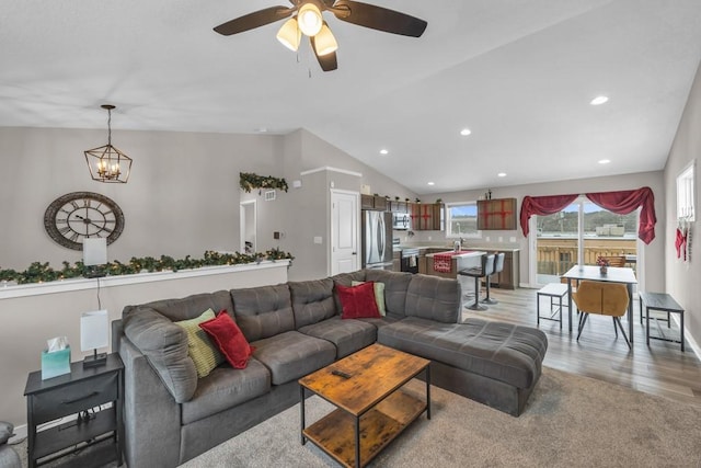 living room with vaulted ceiling, ceiling fan with notable chandelier, and light wood-type flooring