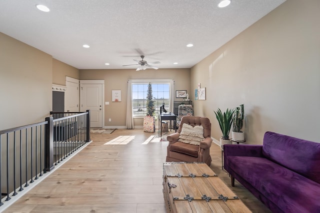 living room with ceiling fan, a textured ceiling, and light wood-type flooring