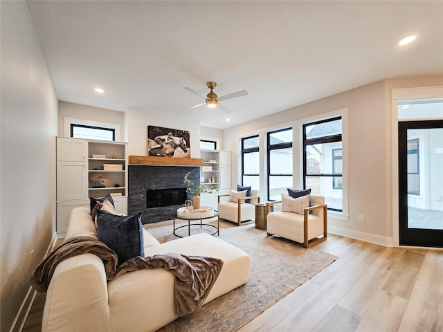 living room featuring a stone fireplace, ceiling fan, and light hardwood / wood-style floors