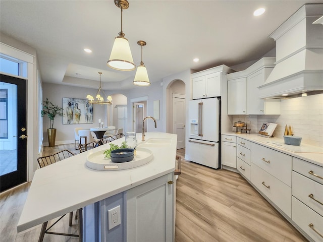 kitchen with a breakfast bar area, pendant lighting, white appliances, and light wood-type flooring