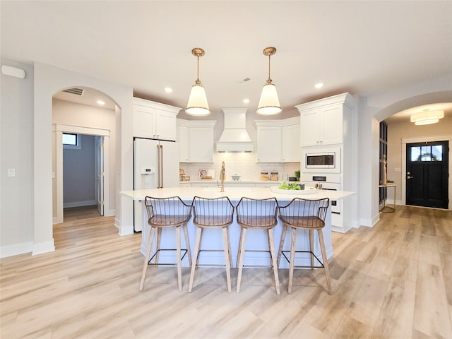 kitchen featuring white cabinets, custom exhaust hood, pendant lighting, and white appliances