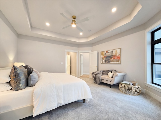 carpeted bedroom with ceiling fan, a tray ceiling, and multiple windows