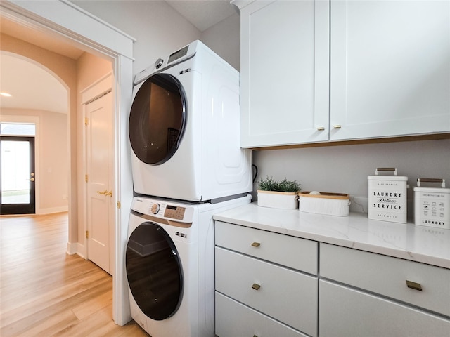 clothes washing area featuring stacked washer and dryer, cabinets, and light hardwood / wood-style flooring