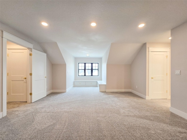 bonus room with a textured ceiling, lofted ceiling, and light carpet