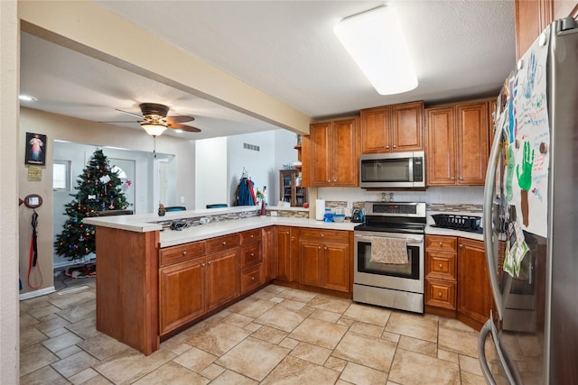 kitchen featuring backsplash, ceiling fan, a textured ceiling, appliances with stainless steel finishes, and kitchen peninsula