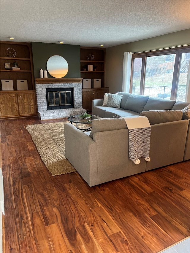 living room featuring a textured ceiling, dark wood-type flooring, built in features, and a fireplace