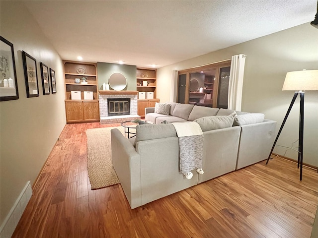 living room featuring a brick fireplace, built in features, a textured ceiling, and light wood-type flooring